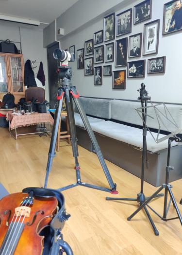Blick in Zimmer, mit Fotoaufnahmen an der Wand. In der Mitte eine Kamera, am linken Rand eine Geige.